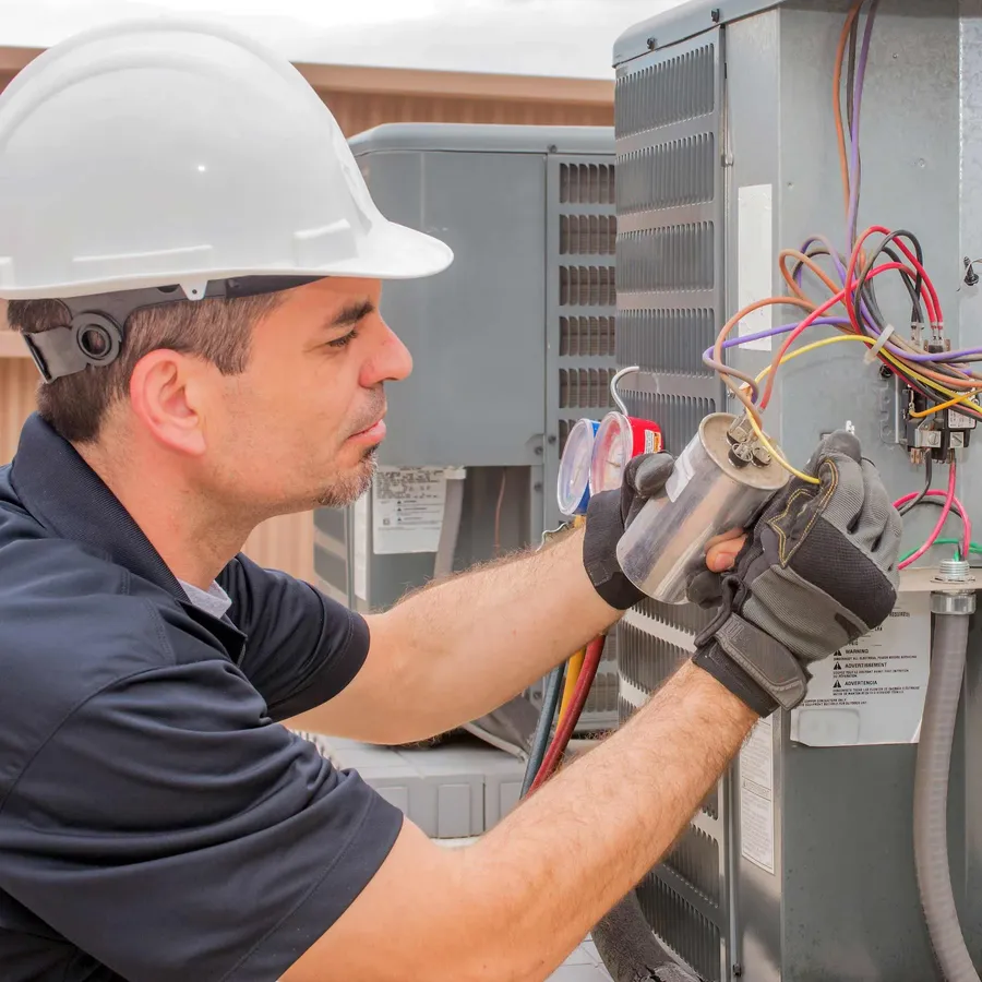 Hands replacing a capacitor in an AC unit.